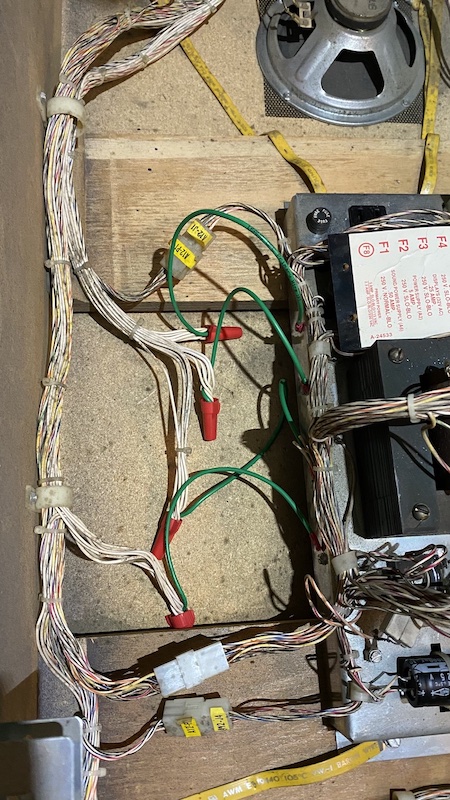A photograph of the inside of a pinball machine with four sets of wires secured in four wire nuts, with green wires connected to a transformer housing
