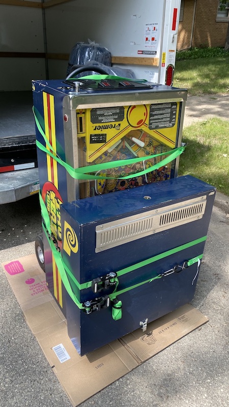A pinball machine with straps around it, folded up in front of a U-Haul truck.