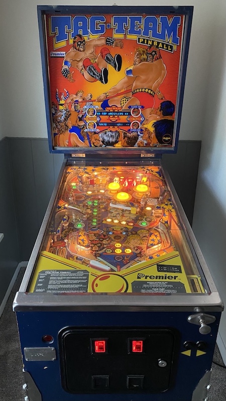 A Tag Team Pinball machine, turned on inside of a room in a house.